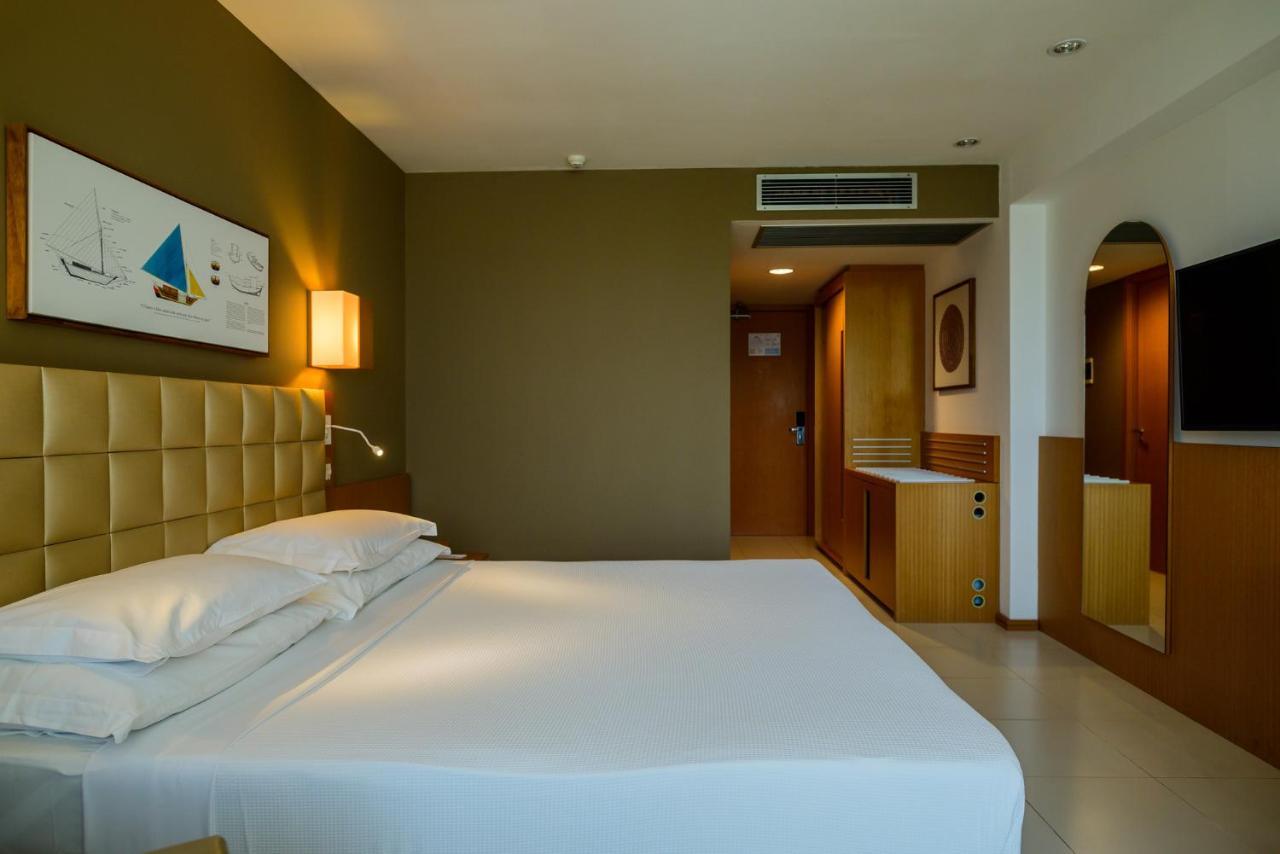 Hotel Luzeiros Sao Luis Eksteriør billede The photo shows a modern hotel room with a simple and elegant design. The room features a large bed with white linens, positioned against a beige upholstered headboard. There is a bedside lamp on one side of the bed. The walls are in soft shades, wit