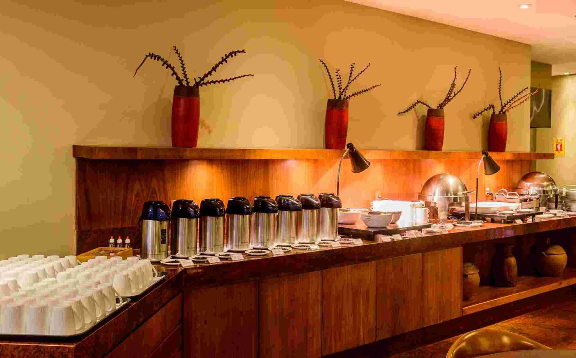 Hotel Luzeiros Sao Luis Eksteriør billede The photo shows a buffet setup in a dining area. There is a long wooden counter that features several items:

1. **Beverages**: Multiple stainless steel coffee or tea containers are lined up, suggesting a beverage station.
2. **Dishware**: There are 