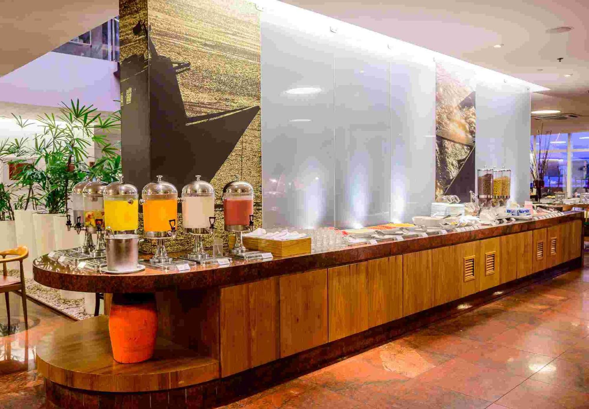 Hotel Luzeiros Sao Luis Eksteriør billede The photo shows a buffet setup in a restaurant or hotel. There's a long wooden counter where various food items and drinks are displayed. Clear containers hold different types of beverages, likely juices or teas, and there are additional food items o