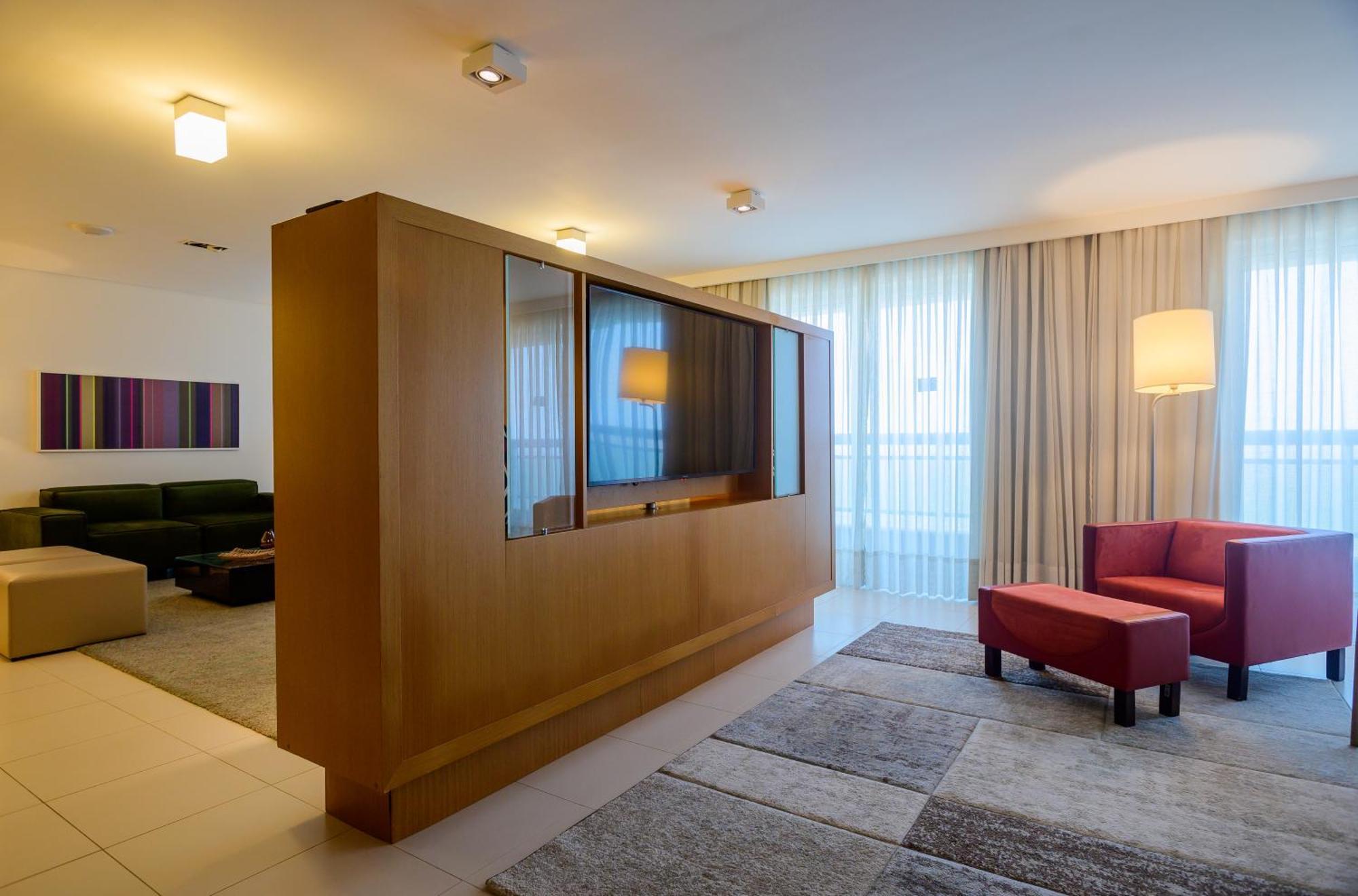 Hotel Luzeiros Sao Luis Eksteriør billede The photo shows a modern living space with a clean and minimalistic design. On the left side, there is a large wooden partition that features glass panels, separating different areas of the room. Beyond the partition, there's a green seating area wit