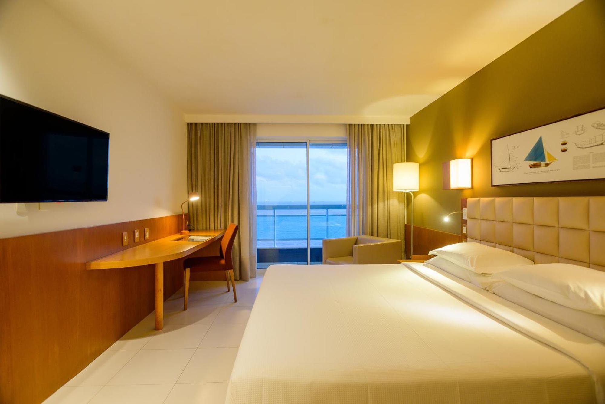 Hotel Luzeiros Sao Luis Eksteriør billede The photo shows a modern hotel room with a bright and inviting atmosphere. The room features a large bed with white linens, a bedside table, and warm lighting. There is a desk and a chair positioned near a window that offers a view of the water outsi