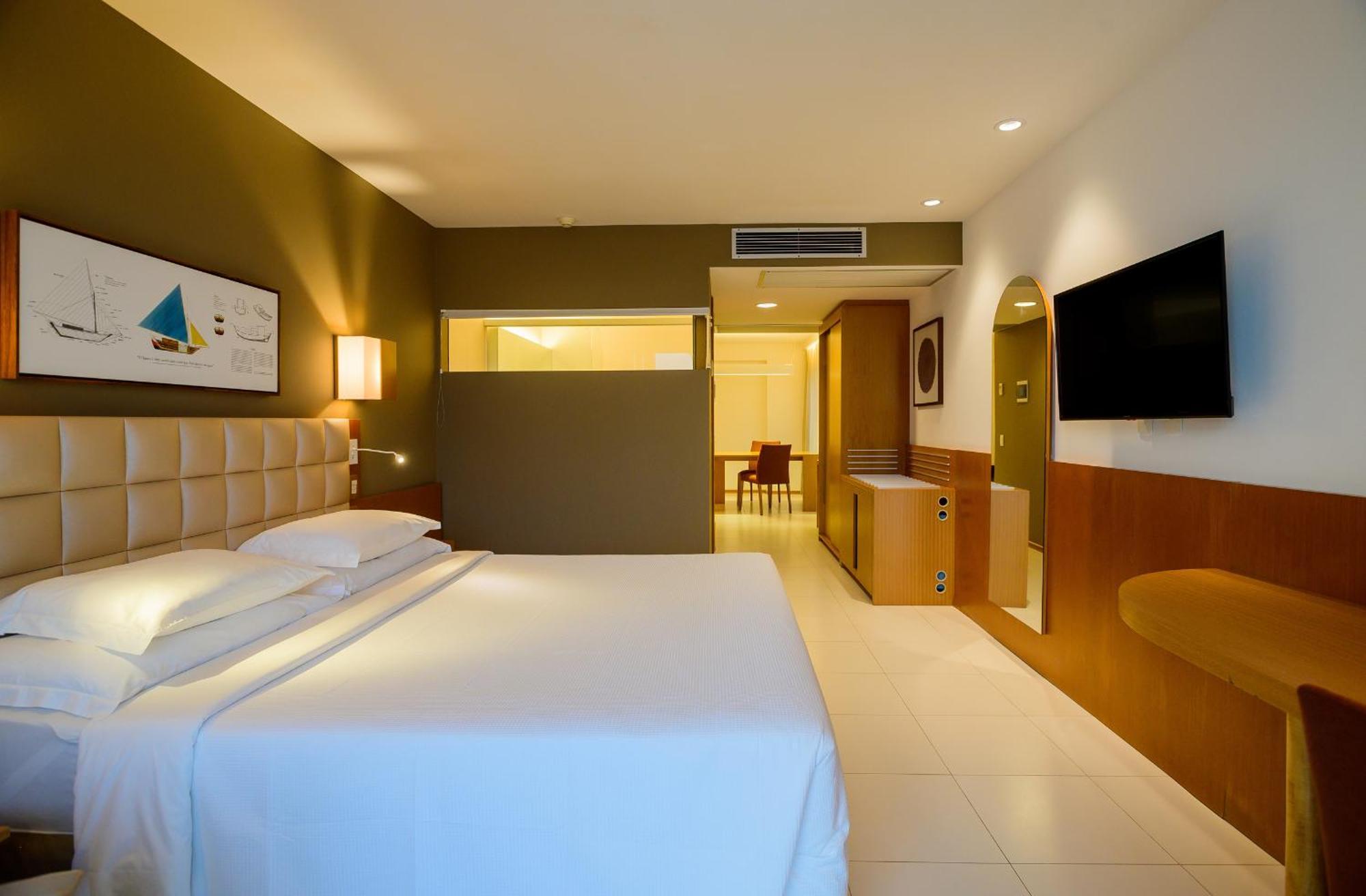 Hotel Luzeiros Sao Luis Eksteriør billede The photo shows a modern hotel room featuring a neatly made bed with white linens. The room has neutral-colored walls, including a dark green accent wall. There is a piece of artwork above the bed, depicting a sailboat scene. To the right, a flat-scr