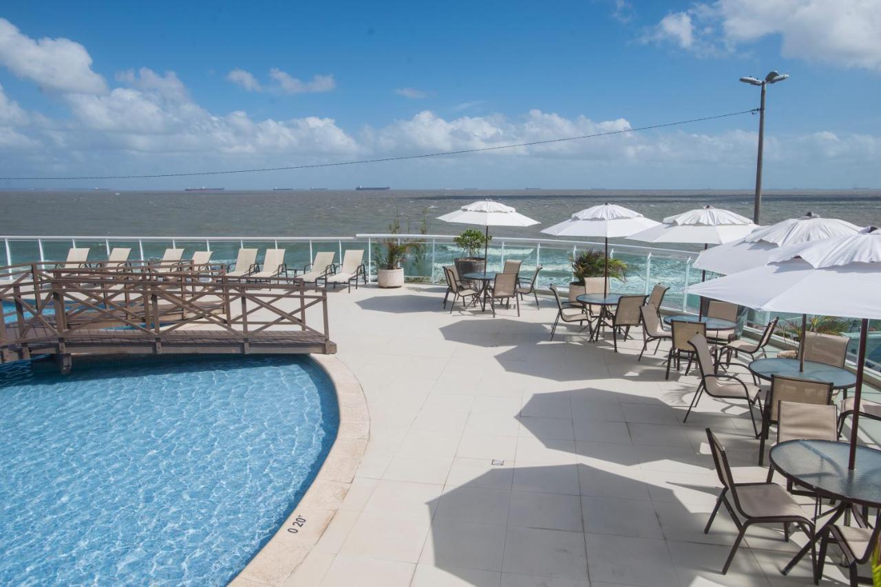 Hotel Luzeiros Sao Luis Eksteriør billede The photo shows a pool area with a clear blue swimming pool surrounded by a deck. There are several lounge chairs and tables set up with umbrellas, providing shade. In the background, you can see the water beyond the pool, likely an ocean or large bo